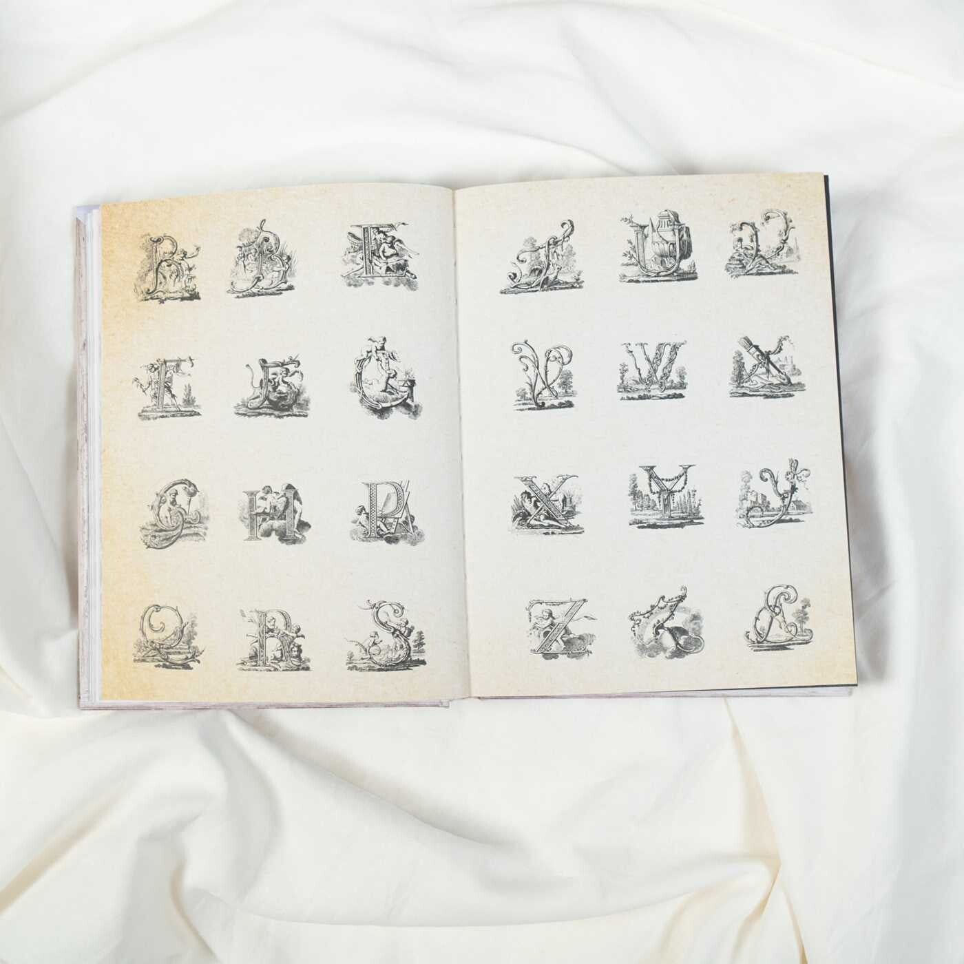 Open book with illustrations of letters on a white fabric background