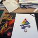 Colorful geometric design on a white sheet of paper and art supplies in the background.