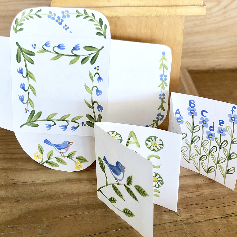 Set of mini cards with floral and bird designs and alphabets on a wooden surface