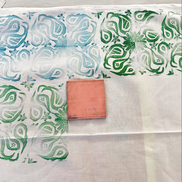 Textile with green and blue patterns and a pink block on a white background