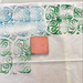 Textile with green and blue patterns and a pink block on a white background