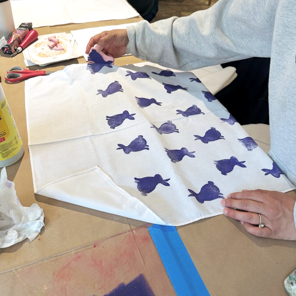 Person working on a stamping project with purple rabbit patterns on white fabric.