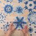 Paper snoflakes dip-dyed in indigo ink displayed on a table with one held in two hands