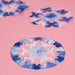 3 paper snoflakes dip-dyed in indigo ink displayed on a pink background