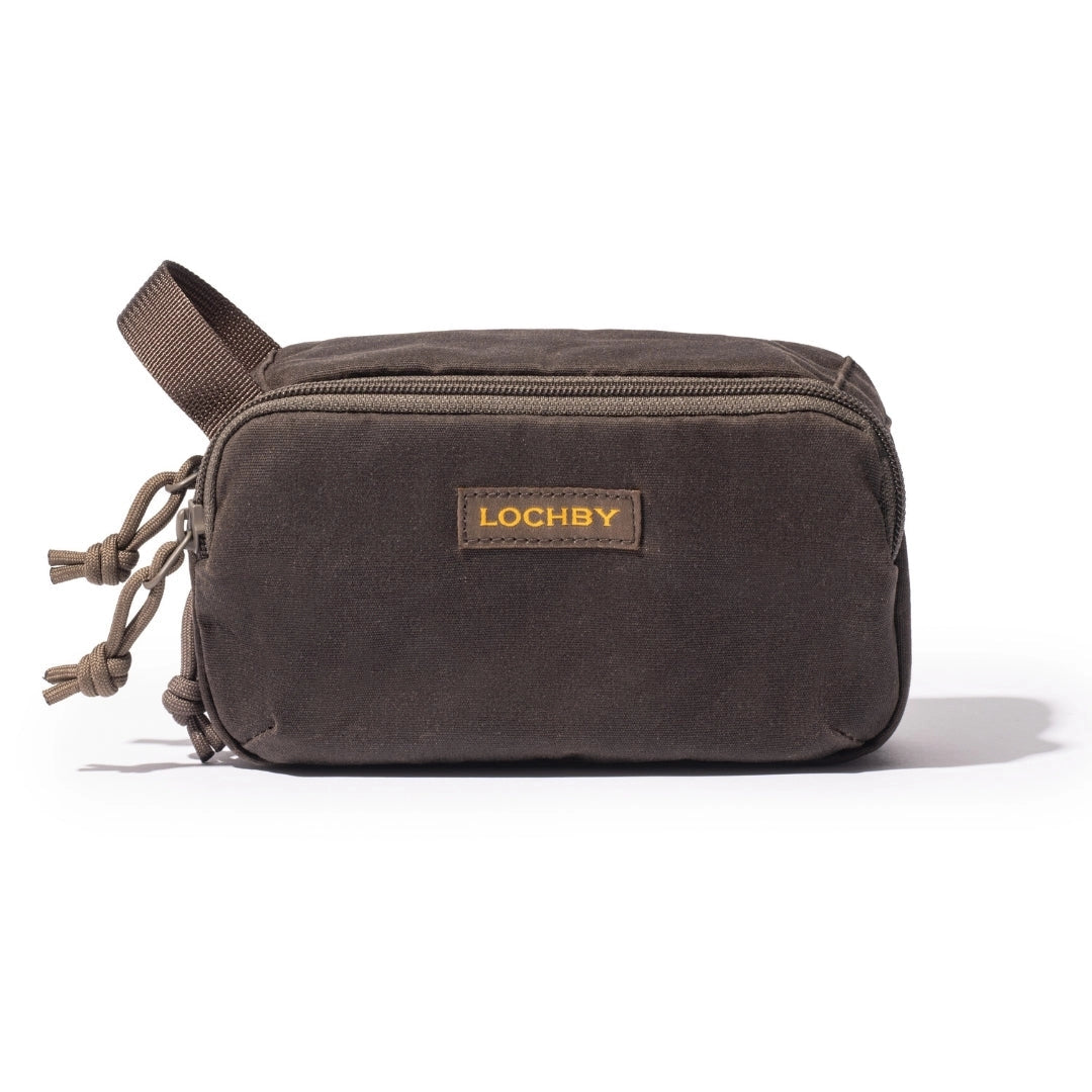 A dark brown canvas toiletry bag with a top zipper, a brown webbing handle, and a tan leather patch with gold lettering that reads 'LOCHBY'.