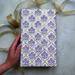 Block Printed lavender and green floral pattern with gold arches used to wrap a gift. Shown with a hand and gold ribbon.