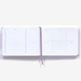 An open white weekly planner style page for swatching daily watercolors  with minimalist gray printed layouts and a thin gray ribbon bookmark, photographed on a clean white background.