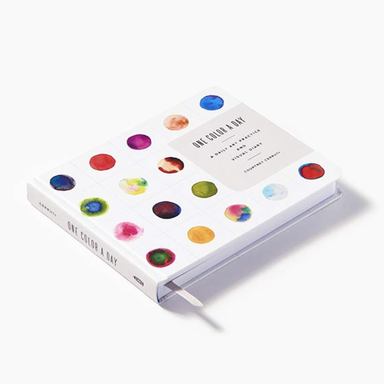 A hardcover art journal titled 'One Color a Day' by Courtney Cerruti, featuring a white cover decorated with colorful watercolor paint swatches and a white ribbon bookmark, set against a clean white background.