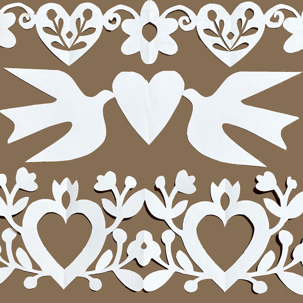 White paper cutout designs featuring two doves with a heart between them, surrounded by ornate heart and floral patterns, displayed on a solid brown background.
