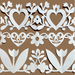 White paper cutout decorative border with hearts, flowers, leaves, and tulips arranged in horizontal rows on a solid brown background.