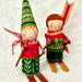 Two handcrafted wooden gnome dolls dressed in colorful winter clothing, standing on wooden skis against a white textured fabric background.