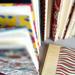 A close-up, angled view of a stack of patterned books, showing colorful spines and covers in red, yellow, blue, beige, and striped designs.